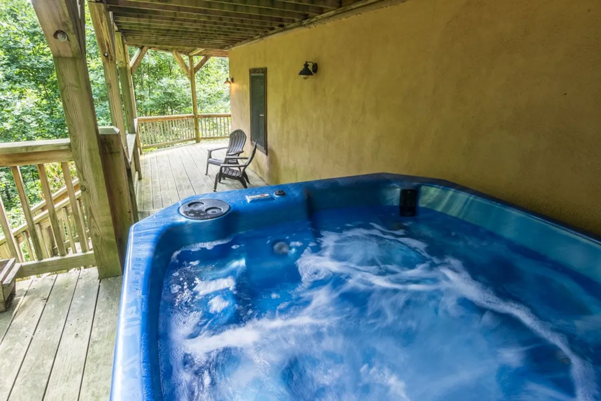 The image shows a hot tub set on a wooden deck overlooking vibrant green foliage, evoking a serene, private retreat nestled in nature. The scene is calm and inviting, ideal for unwinding after a day of adventure or socializing under the stars.