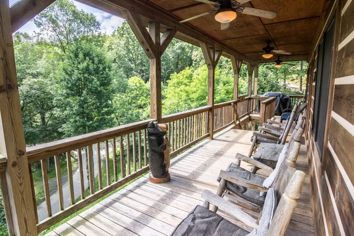 A welcoming wooden deck with rocking chairs and a charming carved bear statue overlooks lush greenery, providing a space for guests to relax, socialize, or watch for wildlife. The spacious deck offers a comfortable spot to enjoy both sunrises and sunsets, echoing themes of family and togetherness.