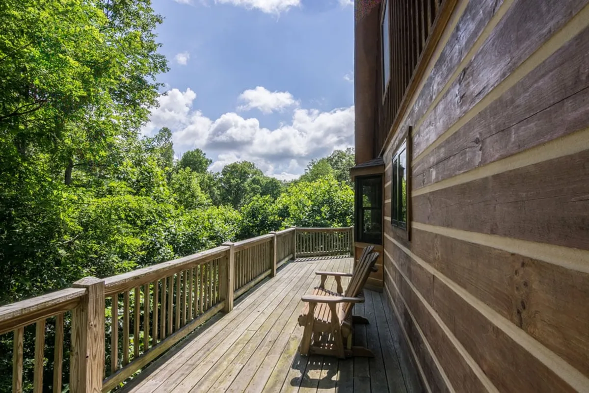 This exterior image features a wooden deck set against lush greenery and a cloudy sky. The deck offers a peaceful vantage point to soak in the surrounding natural beauty, with ample space for outdoor relaxation and enjoyment.