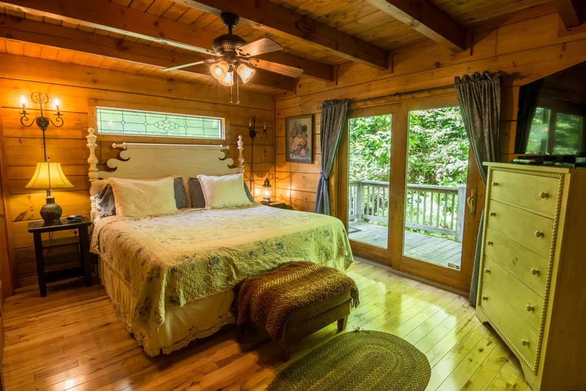 A bright, serene bedroom with a comfortable bed, a window letting in natural light, a dresser, lamp, and artwork. The gentle sunlight and understated decor create a peaceful, restful vibe.