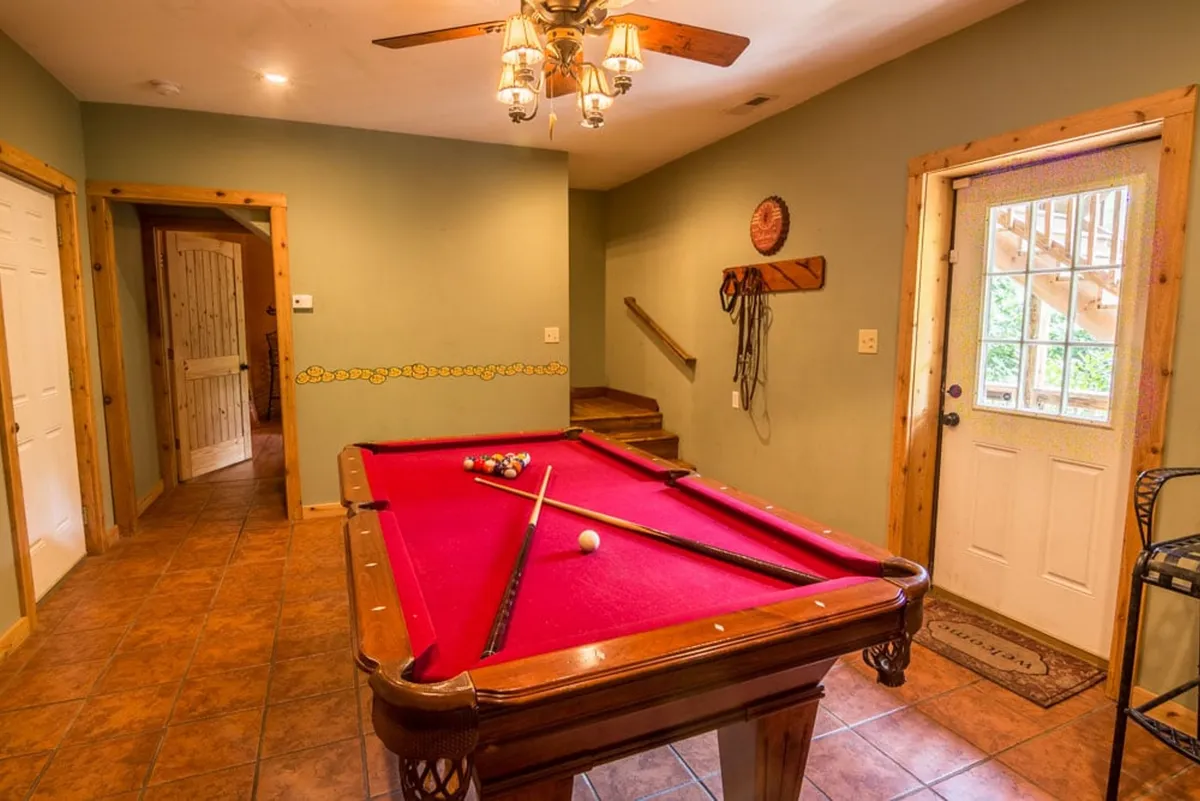 This interior image captures a pool table under a modern light fixture, with an entrance door in the background. The setup suggests a dedicated space for games and gatherings, inviting moments of laughter and friendly competition.