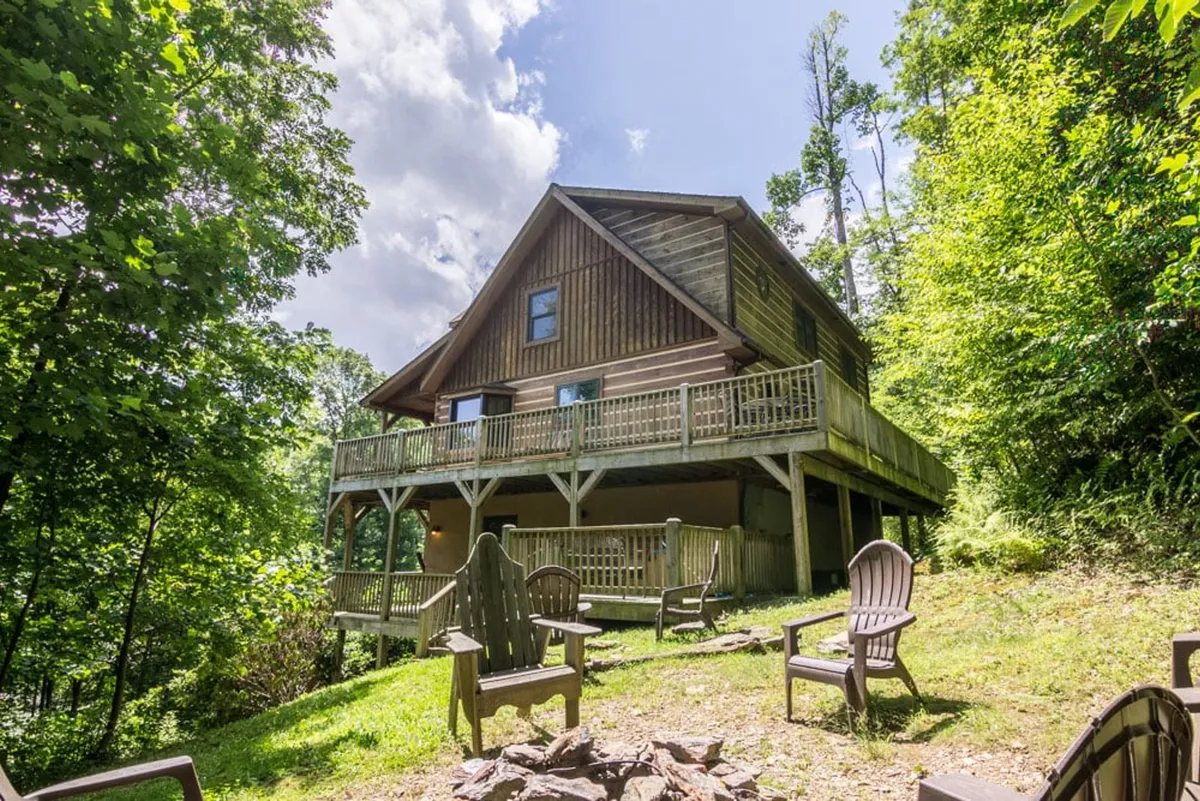 This image captures the exterior of 2 Cubs Cabin, focusing on the inviting wooden house, a spacious deck, and a cozy seating area around the fire pit. The surrounding trees and open yard create an atmosphere perfect for outdoor family gatherings and evenings under the stars.