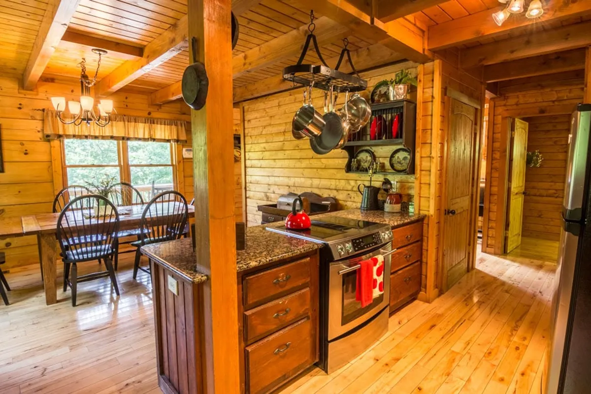 The kitchen is showcased here with a granite-topped island, hanging pots and pans, custom cabinetry, and a dining table in view. A cheerful red kettle on the stove adds a welcoming touch, and the space feels ready for both cooking and conversation.