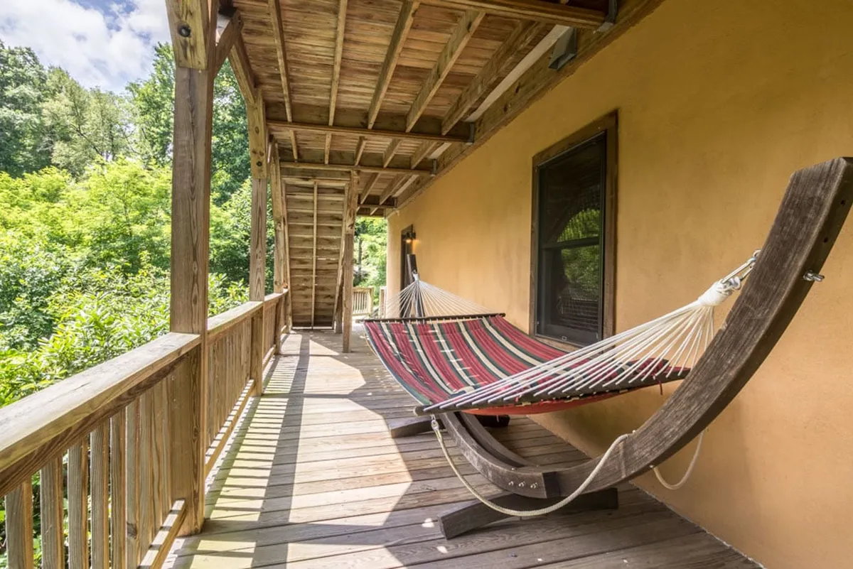 A pair of comfortable hammocks are suspended over a wooden deck, framed by a sturdy railing and enveloped by lush green trees. The view emphasizes relaxation and a connection to the outdoors, with ample natural light and peaceful surroundings.