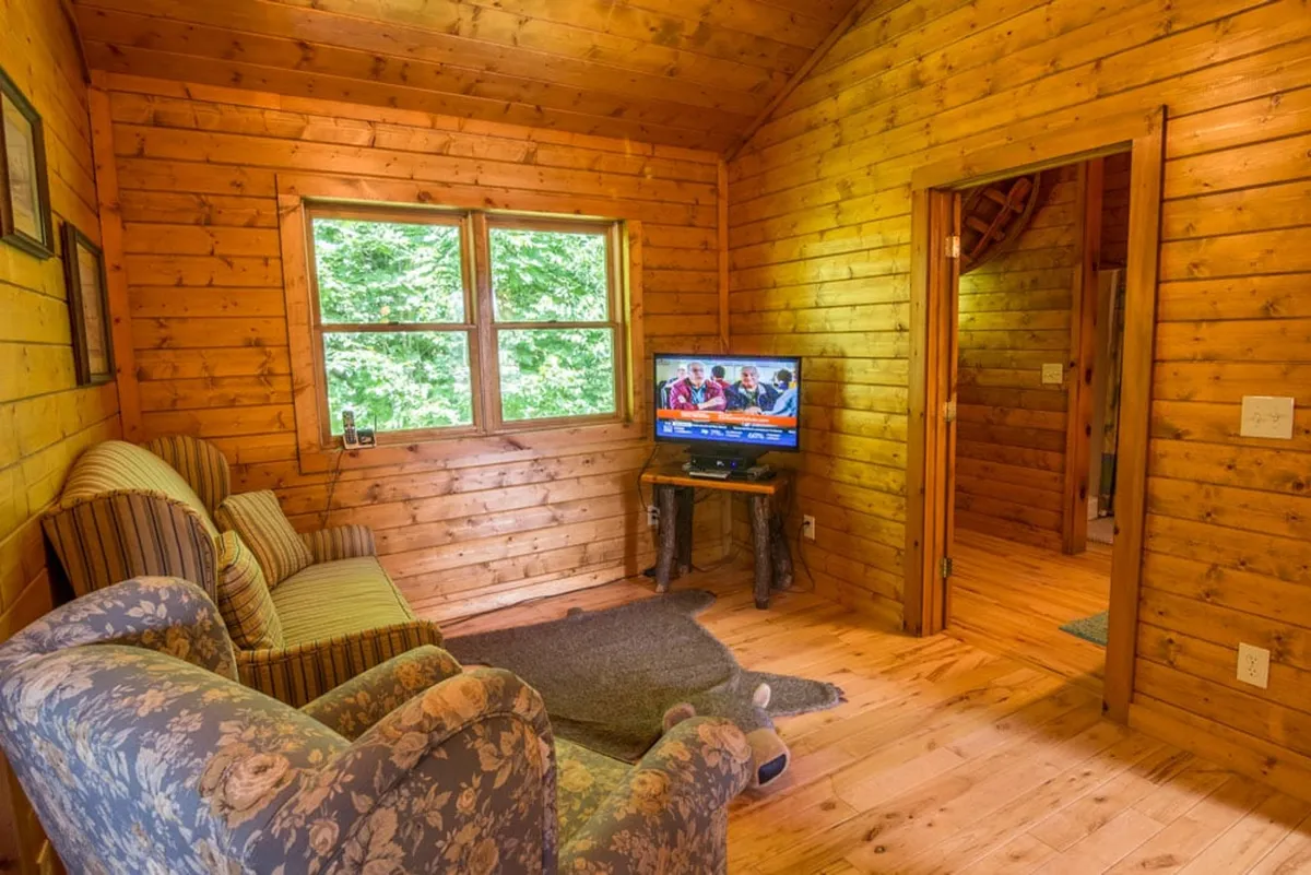 A cozy living area with a comfortable sofa, a television, large windows allowing natural light, and warm wooden walls. The space feels inviting and perfect for watching TV, relaxing after games, or enjoying a quiet moment.
