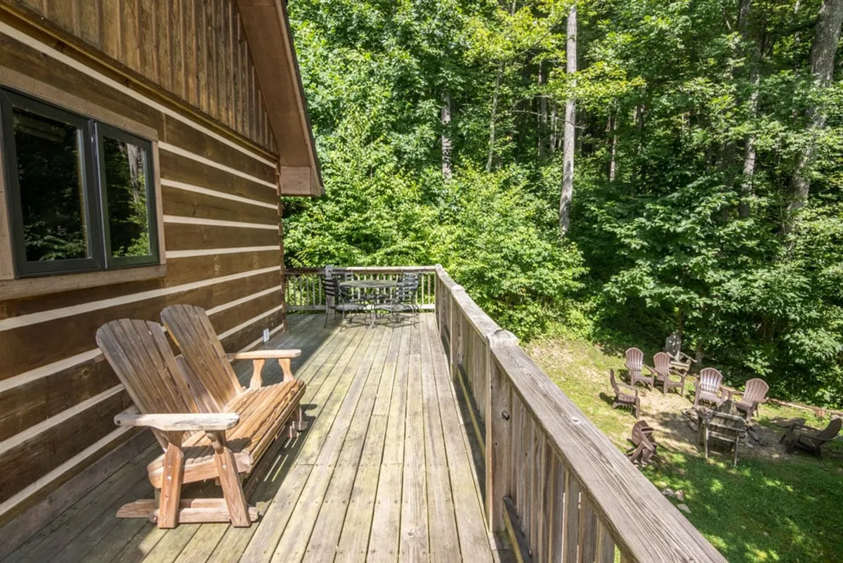 This exterior image features a spacious wooden deck outfitted with adirondack chairs and surrounded by lush greenery. The deck offers a welcoming outdoor seating area ideal for group gatherings, enjoying nature, or hosting evening bonfires with friends.